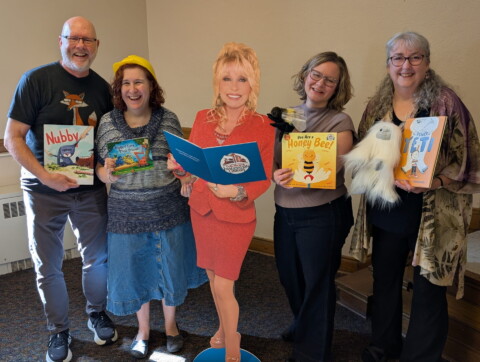 Authors Dan Richards, Brianna Caplan Sayres, Laurie Ann Thompson, and Rebecca Van Slyke holding their Imagination Library books with a cardboard stand-up of Dolly Parton